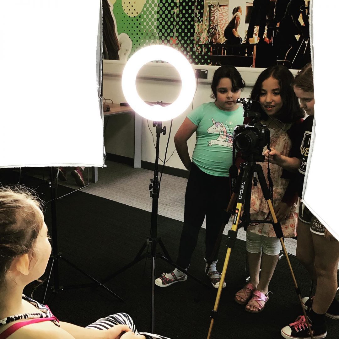 Three members in the Media Room taking a photo of a young person with a digital camera and ring light set up